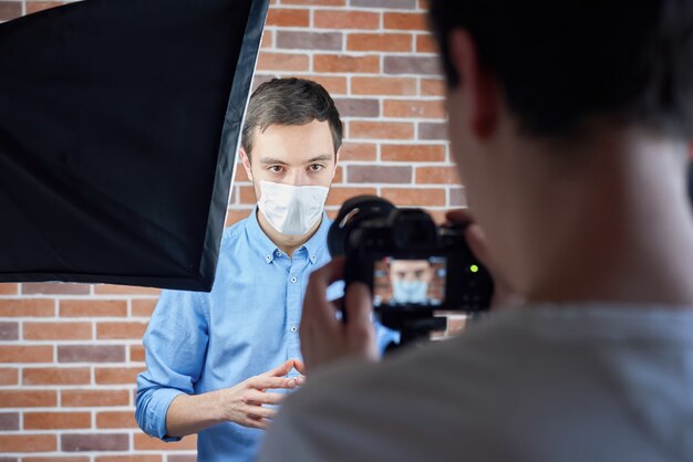 Backstage des kaukasischen Mannes, der mit Kamera in der medizinischen Maske spricht