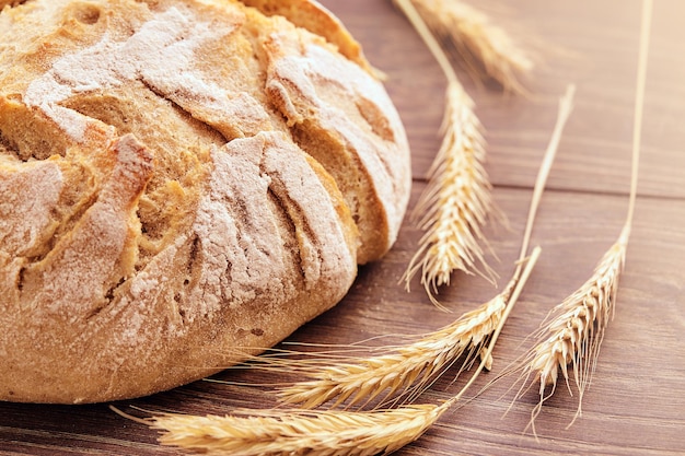 Backwaren isoliert auf einem hölzernen Hintergrund. Frisch gebackenes Brot und Weizenährchen.