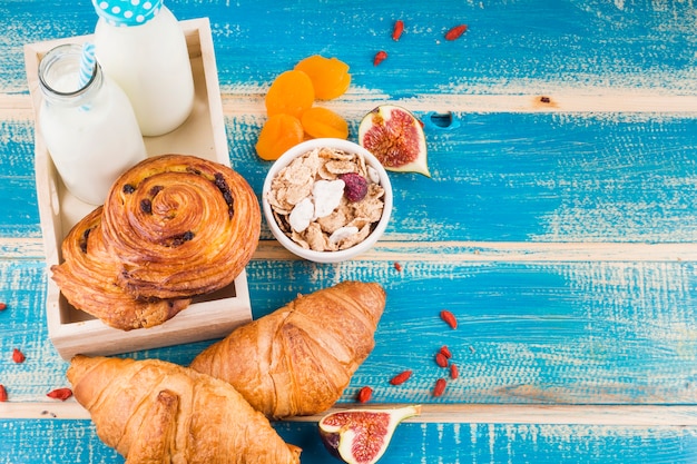 Backwaren mit Milchflaschen; Cornflakes; Feigen- und Trockene Aprikosen über blauem Holzbrett