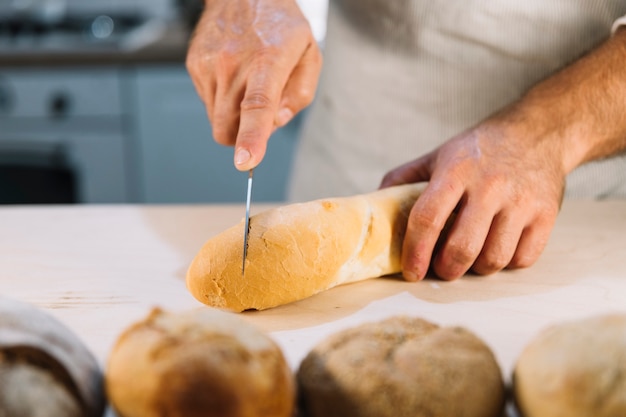 Bäcker, der Brot mit Messer auf Küchenarbeitsplatte schneidet