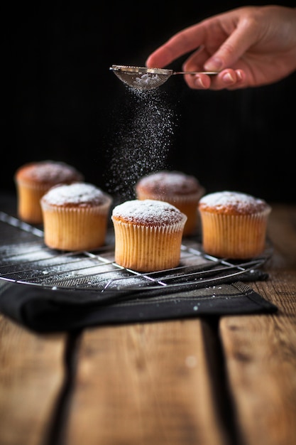 Bäcker, der Puderzucker über Muffins gießt