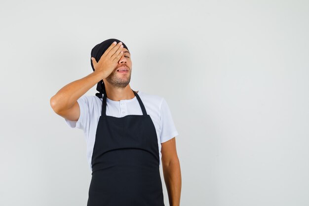 Bäcker Mann im T-Shirt, Schürze, die Hand auf einem Auge hält