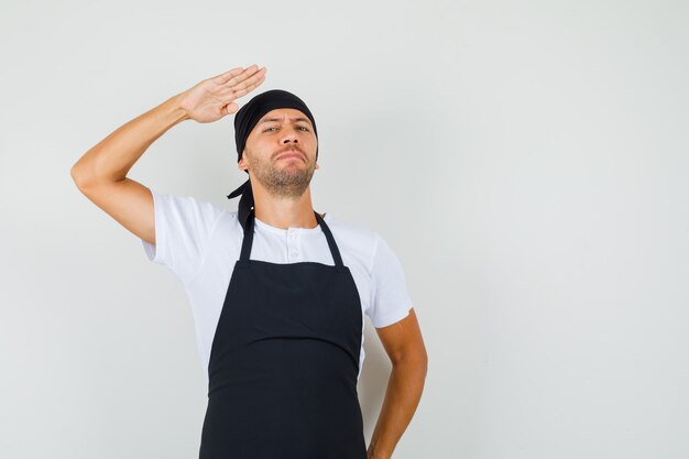 Bäcker Mann im T-Shirt, Schürze zeigt Grußgeste und sieht selbstbewusst aus