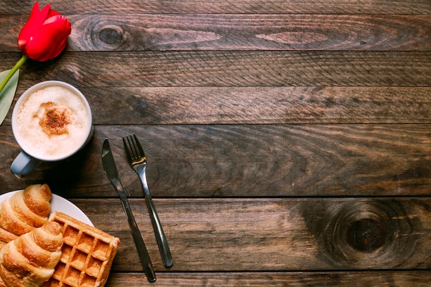 Bäckerei auf Platte in der Nähe von Tasse Getränk, Blumen und Besteck