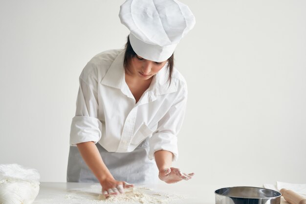 Bäckerin in kochuniform rollt teigmehl professionelles kochen aus. foto in hoher qualität