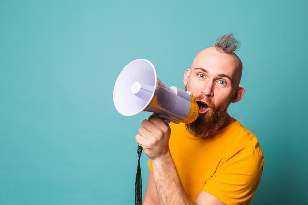 Bärtiger europäischer Mann im gelben Hemd isoliert, verrücktes Geschrei im Megaphonlautsprecher, Aufmerksamkeit!