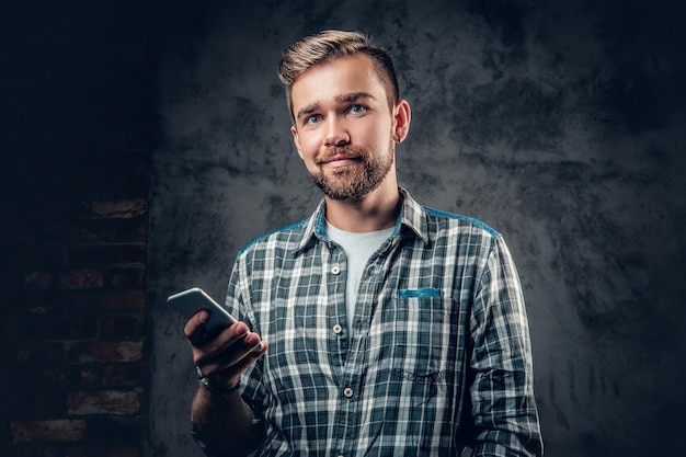 Bärtiger Hipster-Mann in einem Fleece-Shirt hält Smartphone auf grauem Hintergrund.