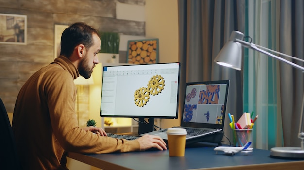 Bärtiger Ingenieur in seinem Heimbüro nachts, der am Getriebe arbeitet.