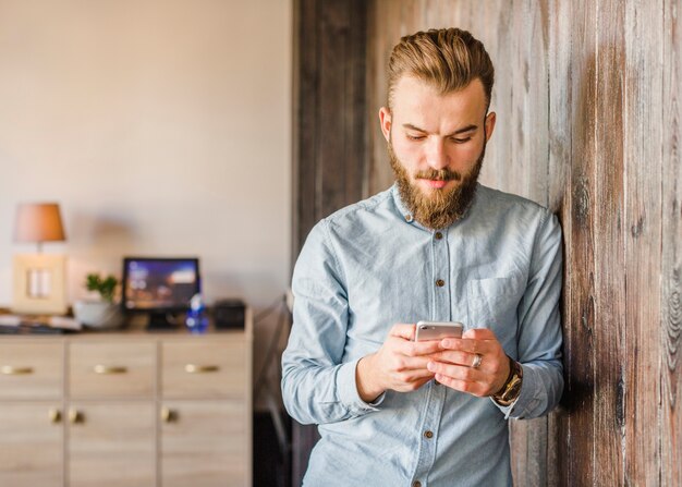 Bärtiger junger Mann, der zu Hause Mobiltelefon verwendet