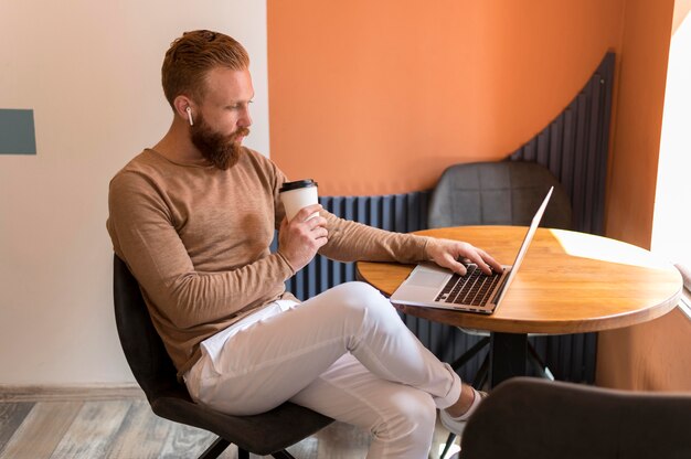 Bärtiger Mann, der an seinem Schreibtisch arbeitet, während er eine Tasse Kaffee hält