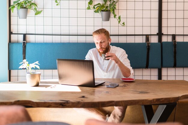 Bärtiger Mann, der eine Tasse Kaffee während der Arbeit hält