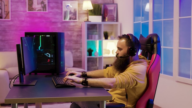 Bärtiger Mann, der Videospiele in einem Raum mit bunten Neonen spielt. Mann, der mit seinen Freunden spricht, während er Videospiele spielt.