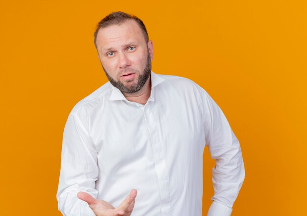 Bärtiger Mann, der weißes Hemd mit ausgestrecktem Arm trägt und über orange Wand steht