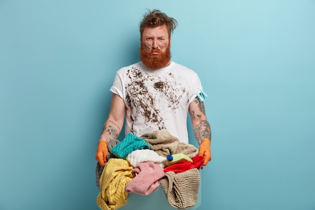 Bärtiger Mann hält Wäschekorb, überwältigt von Hausarbeiten