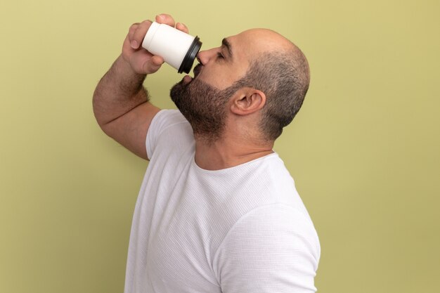 Bärtiger Mann im weißen T-Shirt, der Kaffeetasse hält, die über grüner Wand steht trinken