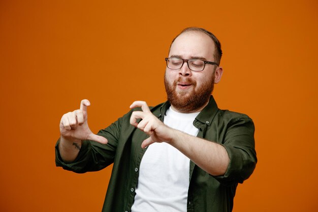 Bärtiger Mann in Freizeitkleidung, der eine Brille trägt und mit den Fingern einen Rahmen macht, der diesen Rahmen mit einem Lächeln im Gesicht betrachtet, das über orangefarbenem Hintergrund steht