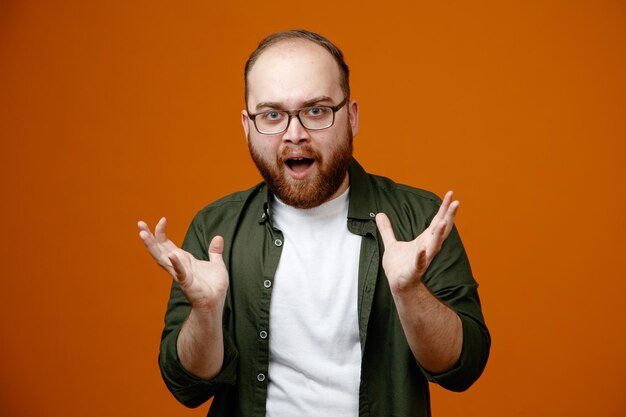 Bärtiger Mann in Freizeitkleidung mit Brille blickt glücklich und aufgeregt in die Kamera und hebt die Arme über orangefarbenem Hintergrund