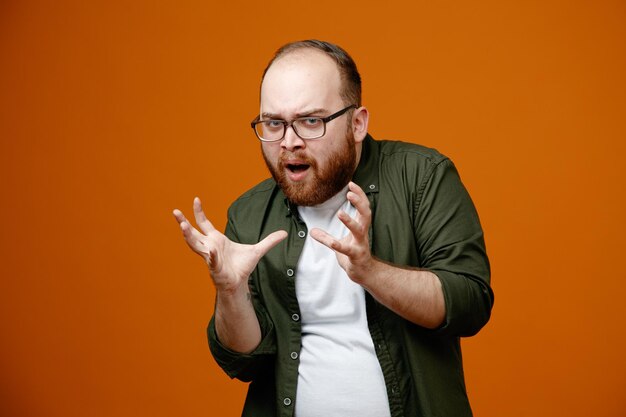 Bärtiger Mann in legerer Kleidung mit Brille, der in die Kamera blickt und erschreckend die Arme hebt, die über orangefarbenem Hintergrund stehen