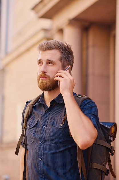 Bärtiger Mann mit Rucksack, der per Smartphone in einer alten europäischen Stadt spricht.