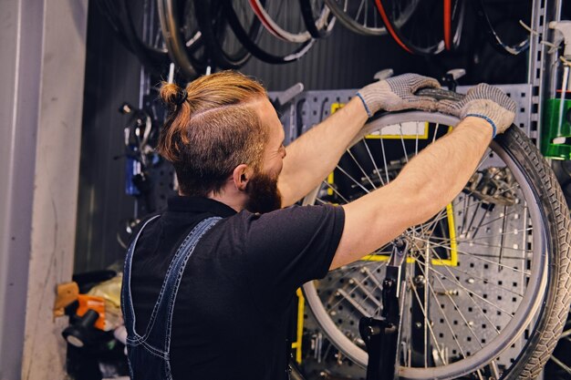 Bärtiger Mechaniker repariert Fahrradreifen in einer Werkstatt. Rückansicht, Serviceanleitung.