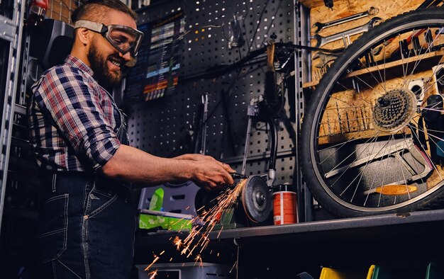 Bärtiger Mechaniker schneidet und poliert Fahrradteile in einer Werkstatt.