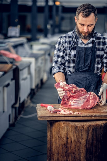 Kostenloses Foto bärtiger metzger, gekleidet in ein fleece-shirt, schnitt frisches speckfleisch.