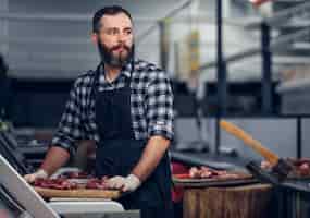 Kostenloses Foto bärtiger metzger in einem fleecehemd, der auf einem markt frisch geschnittenes fleisch serviert.