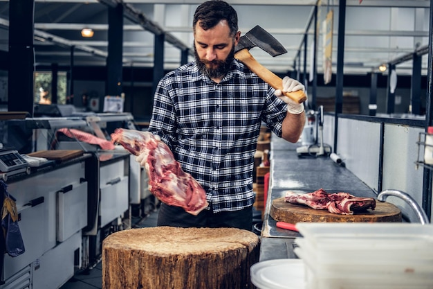 Kostenloses Foto bärtiger metzger in einem fleecehemd schneidet fleisch mit einer blutigen axt.