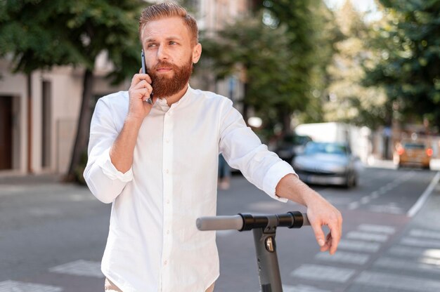 Bärtiger moderner Mann der Vorderansicht, der auf dem Roller am Telefon spricht