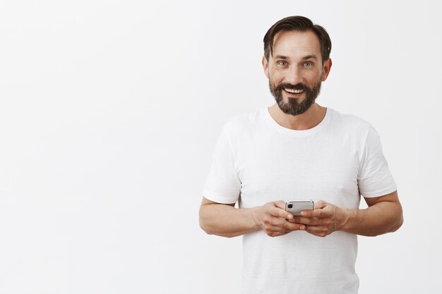 bärtiger reifer Mann, der mit seinem Telefon aufwirft