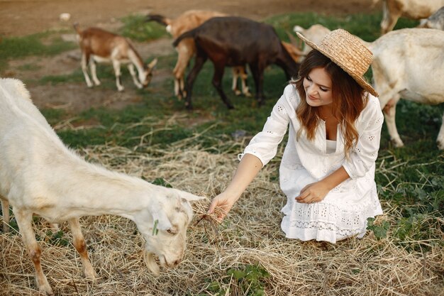 Bäuerin mit weißer Ziege. Grünes Gras der Frau und der kleinen Ziege. Öko-Bauernhof. Bauernhof und Landwirtschaftskonzept. Dorftiere. Mädchen spielen süße Ziege. F.