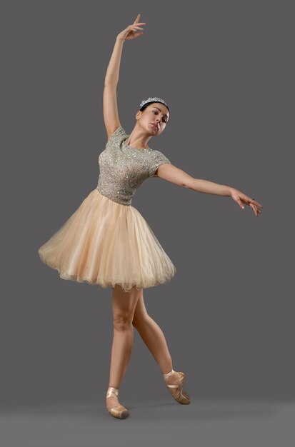 Ballerina in beigem Kleid und Ballettschuhen, die im Studio tanzen