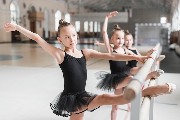 Ballerinamädchen im schwarzen Ballettröckchen, das ihre Beine auf Stange ausdehnt