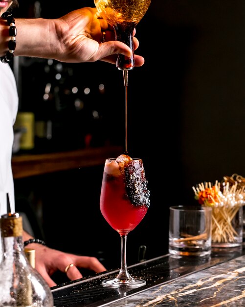 Bar Tender gießt Sirup in rotes Cocktailglas