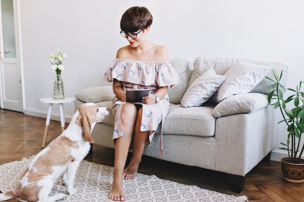 Barfuß lächelndes Mädchen mit weißer Maniküre, die mit Liebe auf Hund nach Arbeit mit Tablette schaut