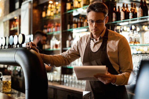 Barista liest Inventarliste, während er hinter der Bartheke arbeitet