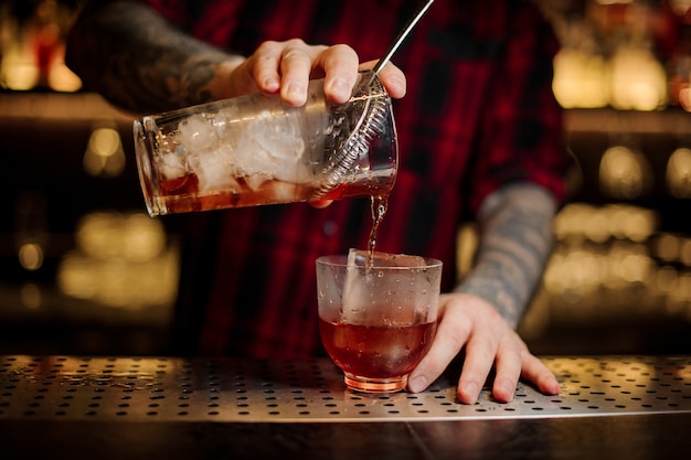 Barkeeper gießt einen leckeren vieux carre cocktail aus dem messbecher in ein glas auf der bartheke