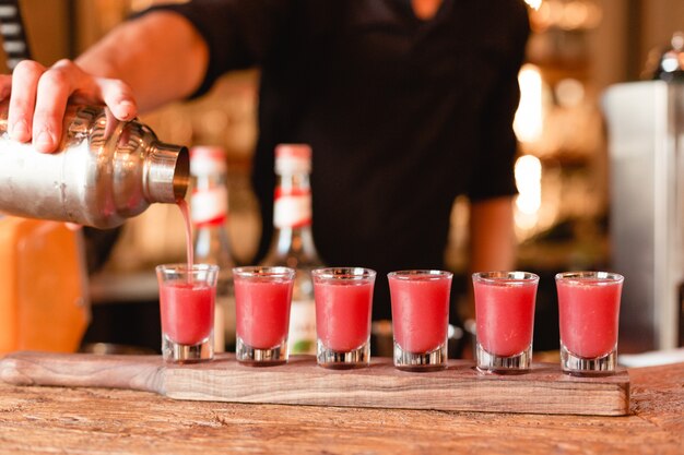 Barmixer, der rote Cocktails in kleine Gläser vom Mixbecher setzt.