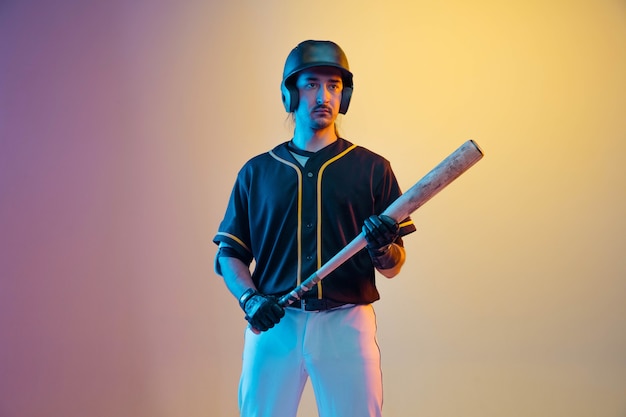Baseballspieler, krug in einer schwarzen uniform, die zuversichtlich auf gradientenwand im neonlicht aufwirft. junger profisportler in aktion und bewegung. gesunder lebensstil, sport, bewegungskonzept.