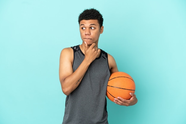 Basketballspieler afroamerikanischer mann isoliert auf blauem hintergrund, der zweifel hat und denkt