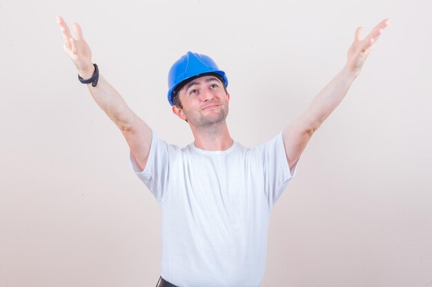 Bauarbeiter im T-Shirt, Helmöffnungsarme für Umarmung und fröhliches Aussehen