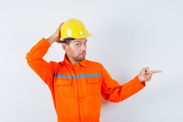 Bauarbeiter in Uniform, Helm zeigt zur Seite und sieht nachdenklich aus, Vorderansicht.