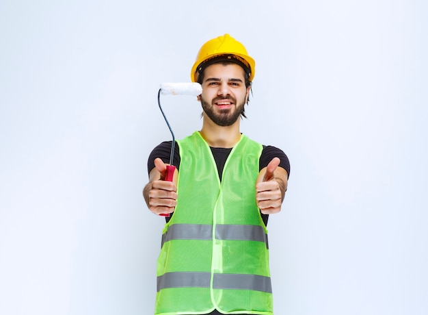 Bauarbeiter mit gelbem helm, der eine weiße zierrolle hält.