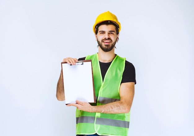 Bauarbeiter mit gelbem Helm, der einen Projektbericht hält.