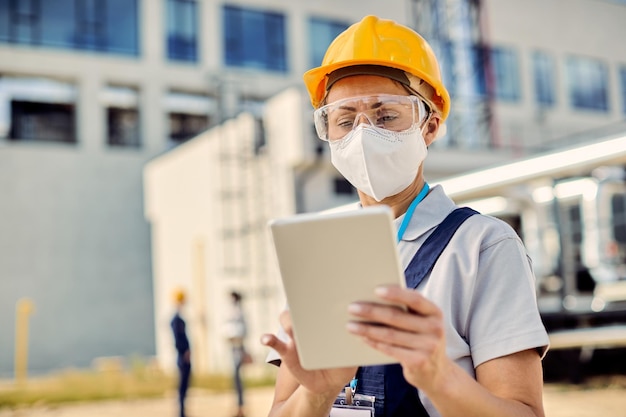 Bauingenieur mit schützender Gesichtsmaske, die auf der Baustelle am Touchpad arbeitet