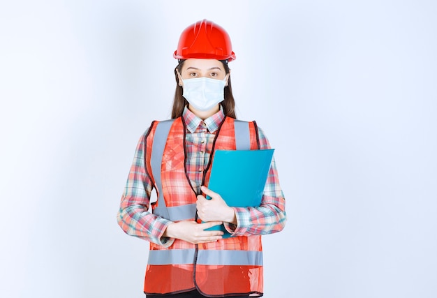 Bauingenieurin in schutzmaske und rotem helm mit blauem ordner