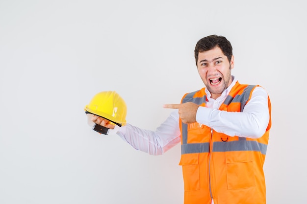 Baumeister Mann schreien, während Finger auf Helm im Hemd, Uniform, Vorderansicht zeigen.