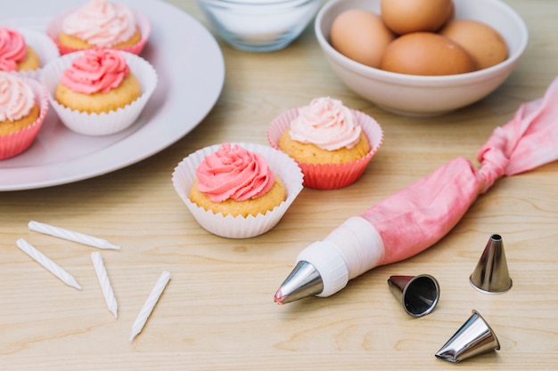 Baumwollbeutel mit Düse; Cupcake; Eier und Kerzen auf Schreibtisch aus Holz