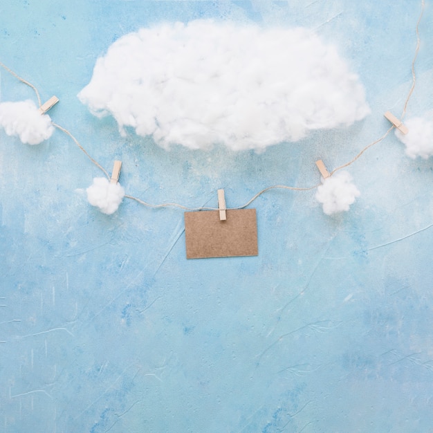 Baumwollwolken über dekorativer brauner Karte hängen mit Wäscheklammern