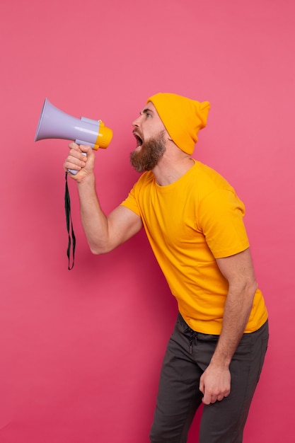 Beachtung! Verärgerter europäischer Mann, der im Megaphon auf rosa Hintergrund schreit